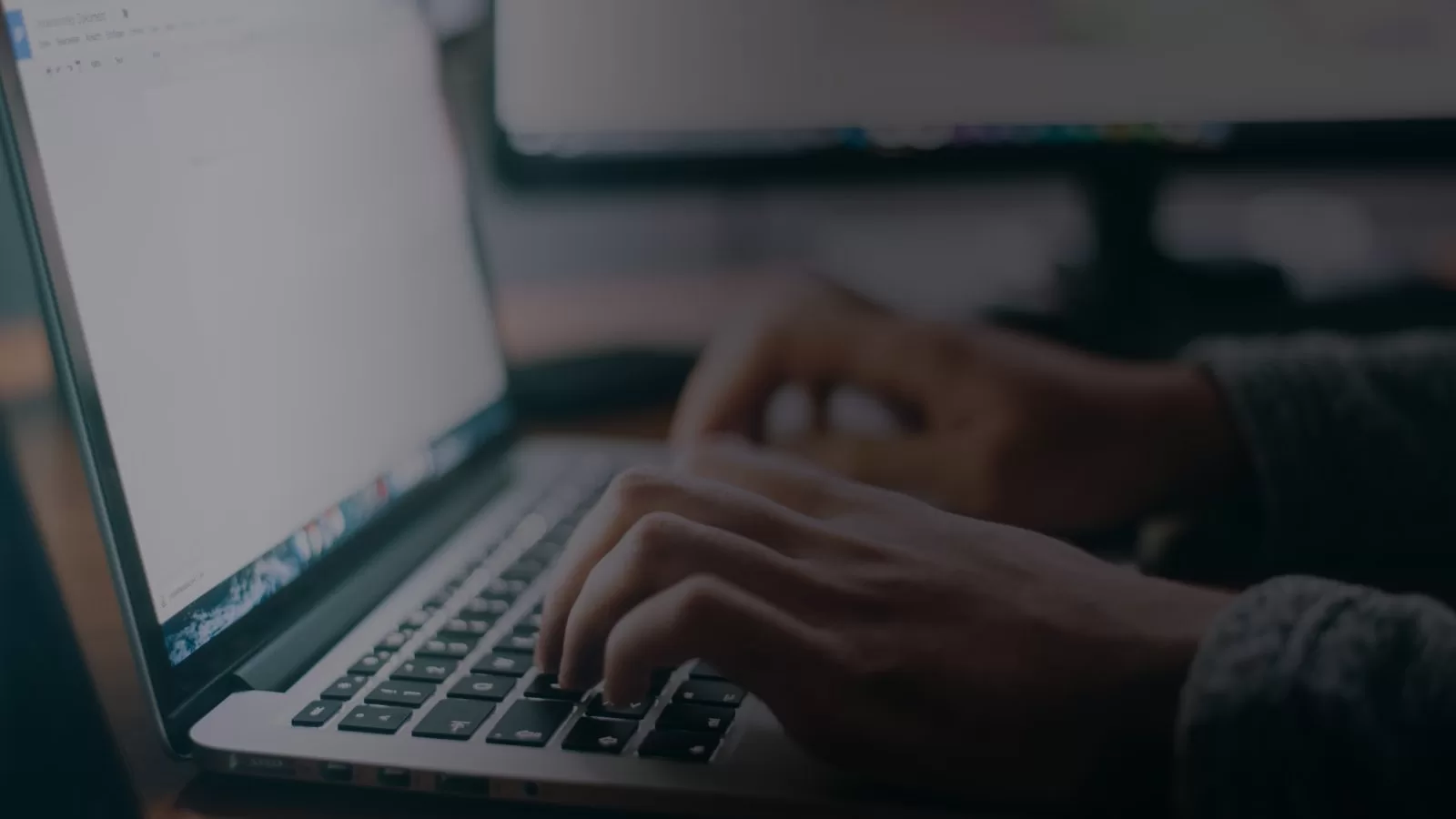 يدان تكتبان على لوحة مفاتيح حاسوب محمول في ضوء خافت