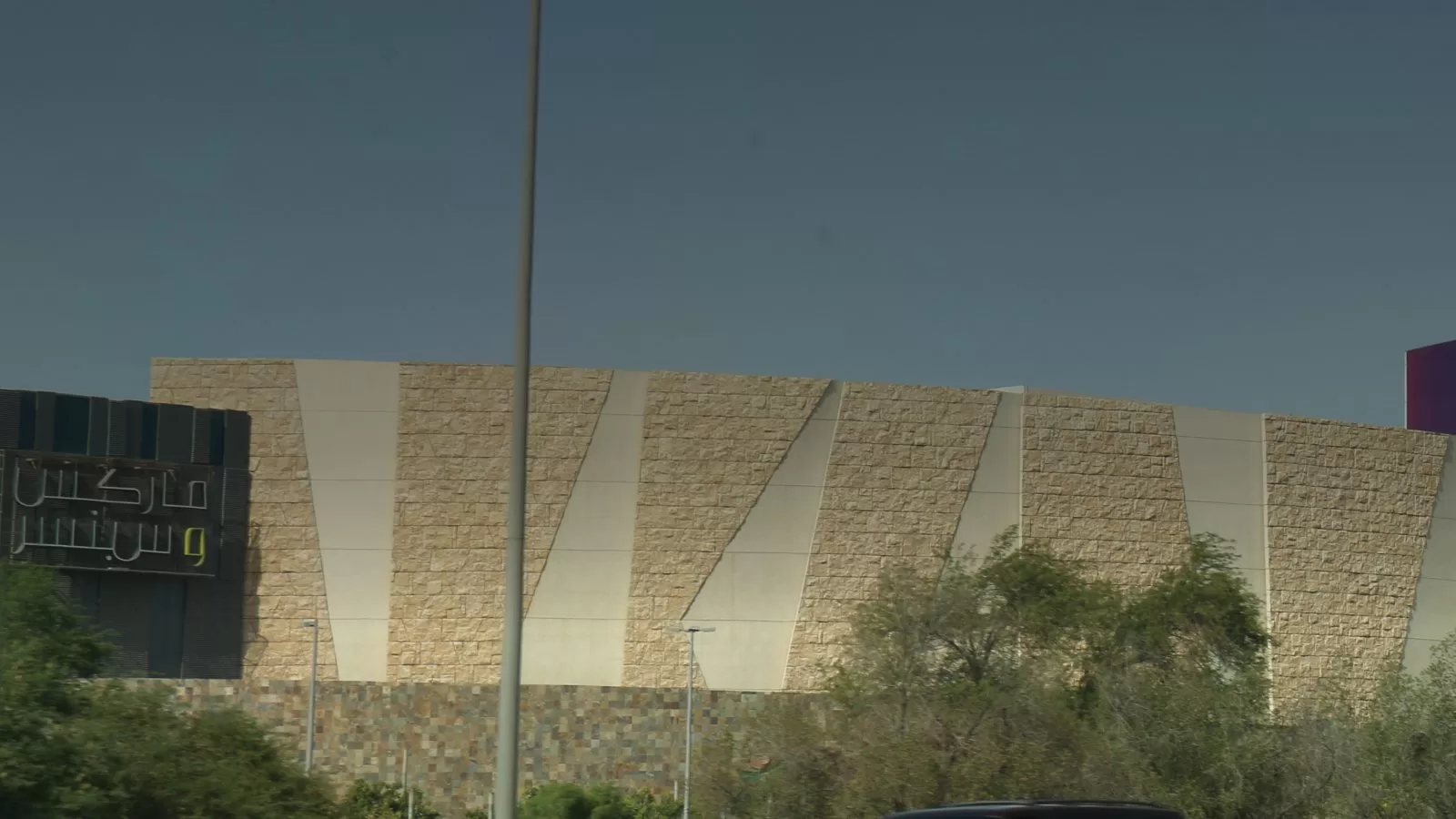 الواجهة الحجرية لمجمع 360 من الطريق، وامامها اشجار وعمود انارة