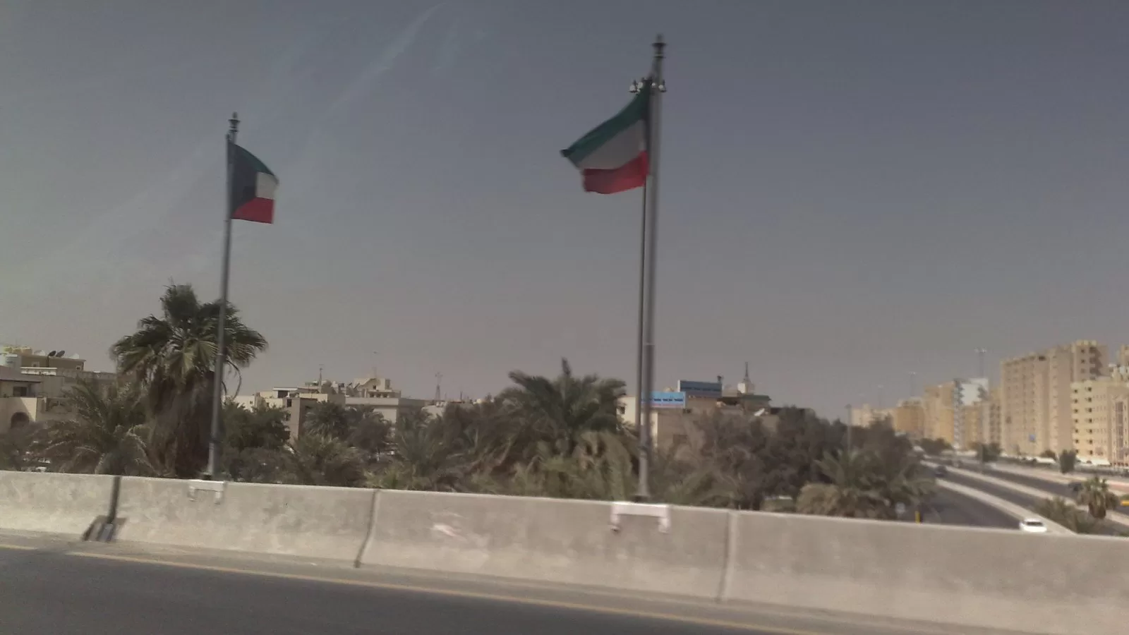 طريق سريع في الكويت وعلما الكويت مرفوعان على جانبه ونخيل خلفهما