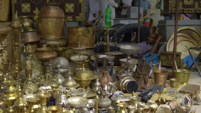بسطة نحاسيات في سوق الجمعة بالشويخ، اوان وقدور ومباخر مرتبة على الارض وبائع جالس خلفها