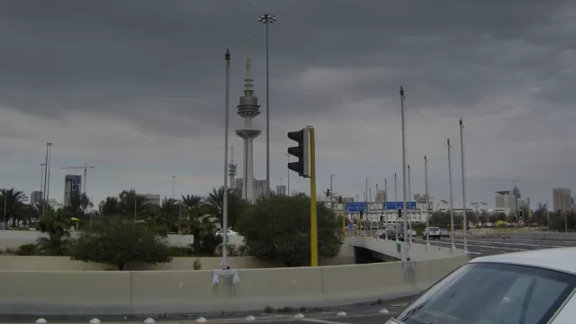 برج التحرير في مدينة الكويت مرئيا من الشارع في يوم غائم، وحوله نخيل واعمدة انارة