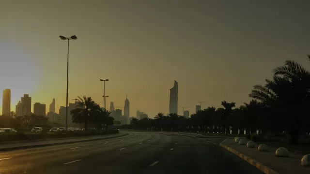 طريق واسع في الكويت عند الغروب وفي نهايته ابراج مدينة الكويت، ونخيل على الجانبين