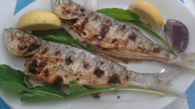 A plate of grilled fish served with lemon on a table