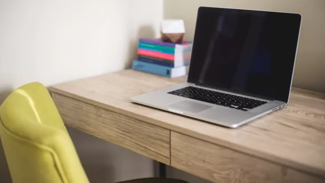 حاسوب محمول مفتوح على مكتب خشبي وبجانبه كتب