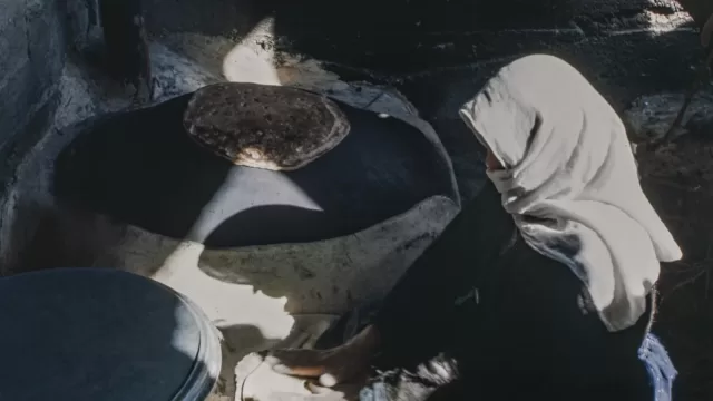 A woman baking thin flatbread on a hot metal griddle