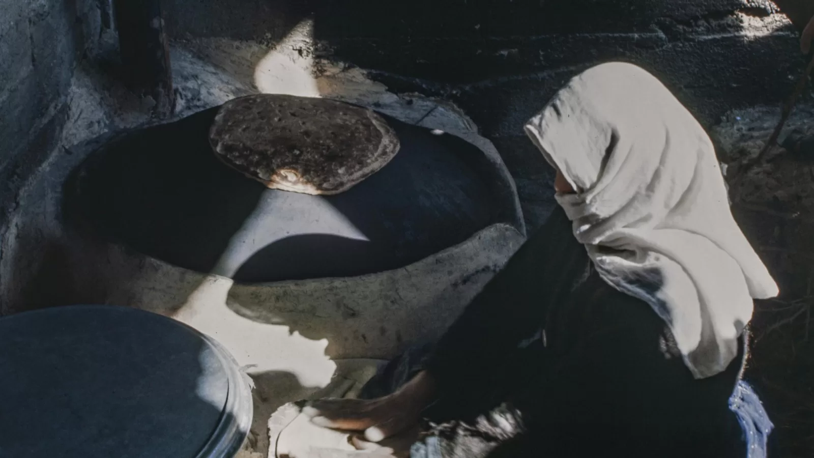 A woman baking thin flatbread on a hot metal griddle